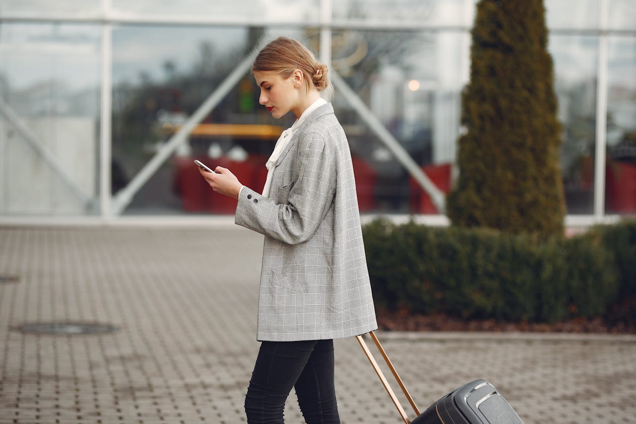 Person looking at a mobile device while walking with a rollingsuitcase
